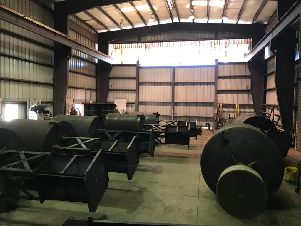 Several bare-steel BL 620 buoy hulls and their tower frames lying on the floor of the Wet Tech fab shop