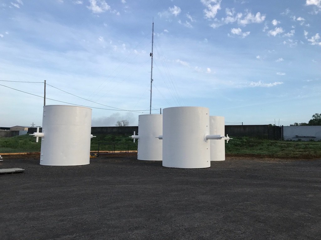 Four white cylindrical steel midline and mooring buoys with pipe stub arms standing in the gravel Wet Tech yard